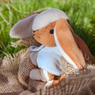 Handmade velveteen bunny with caramel and cream fur and a light blue cloak sitting on sacking with a grass background