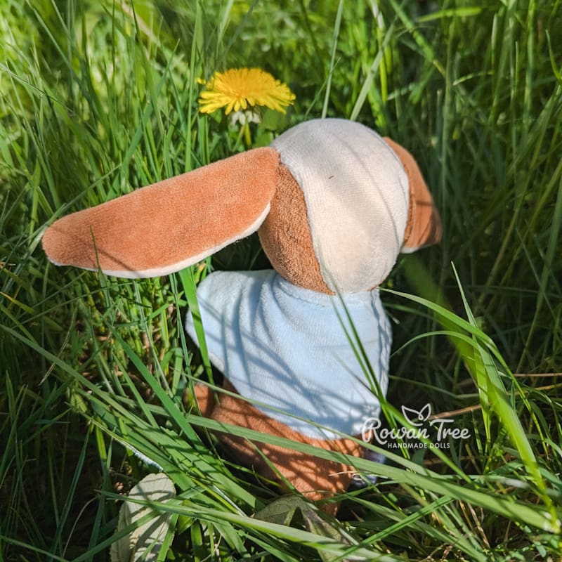 handmade velveteen bunny with caramel and cream fur and long floppy ears viewed from rear, wearing light blue velveteen cape