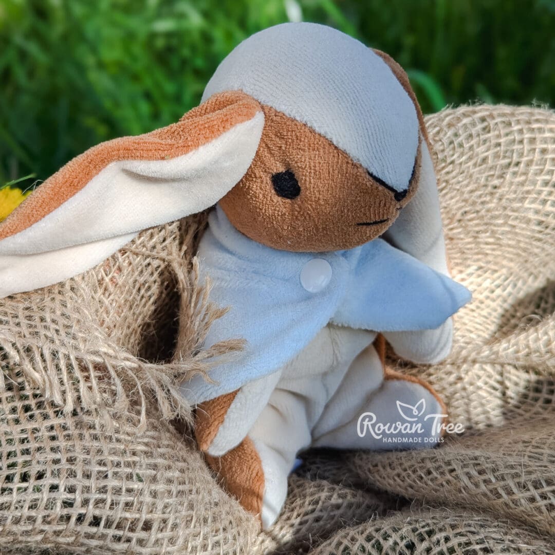 handmade velveteen bunny with blue cloak sat on hessian with garden in background