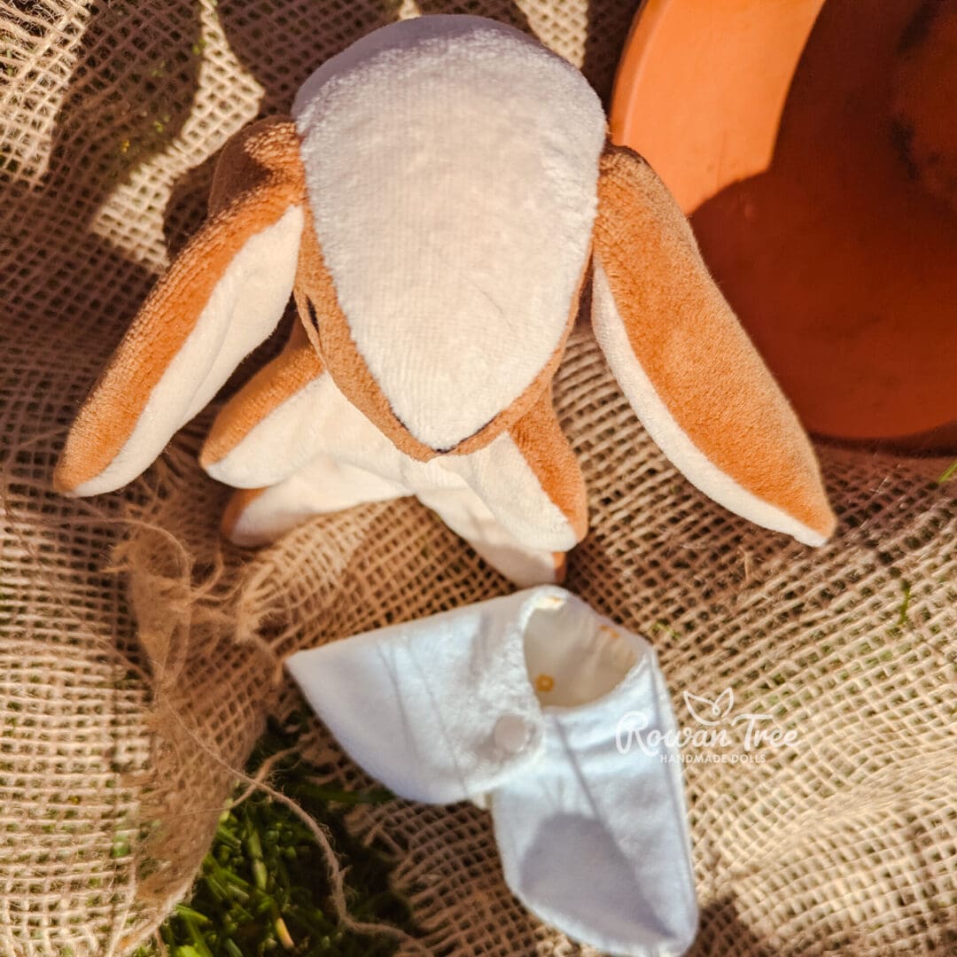 handmade velveteen bunny viewed from top next to light blue velveteen cloak on hessian background