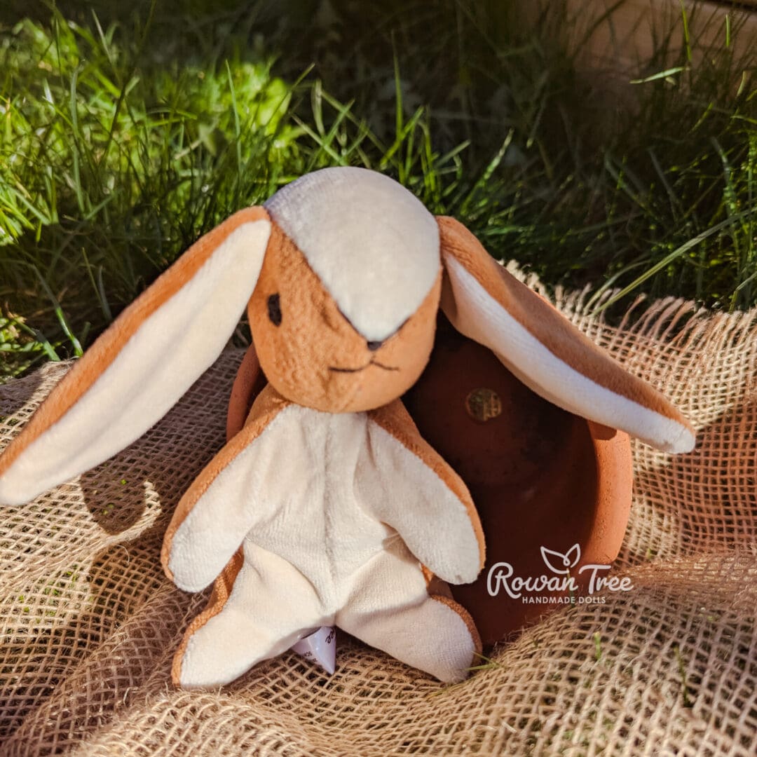 Handmade velveteen caramel and cream bunny sat on hessian in front of plant pot
