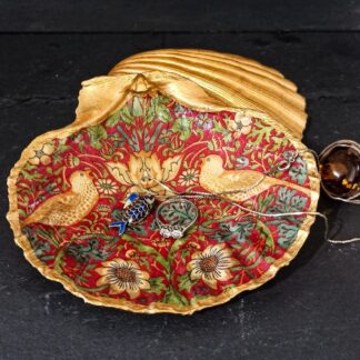 Strawberry Thief scallop shell decoupage trinket dish, depicting the two birds facing each other on a red background. The gilded shell looks striking against a black slate background and jewellery is placed in and around the handmade shell dish.