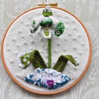 An embroidered stumpwork snowdrop mounted on a 6" embroidery hoop.