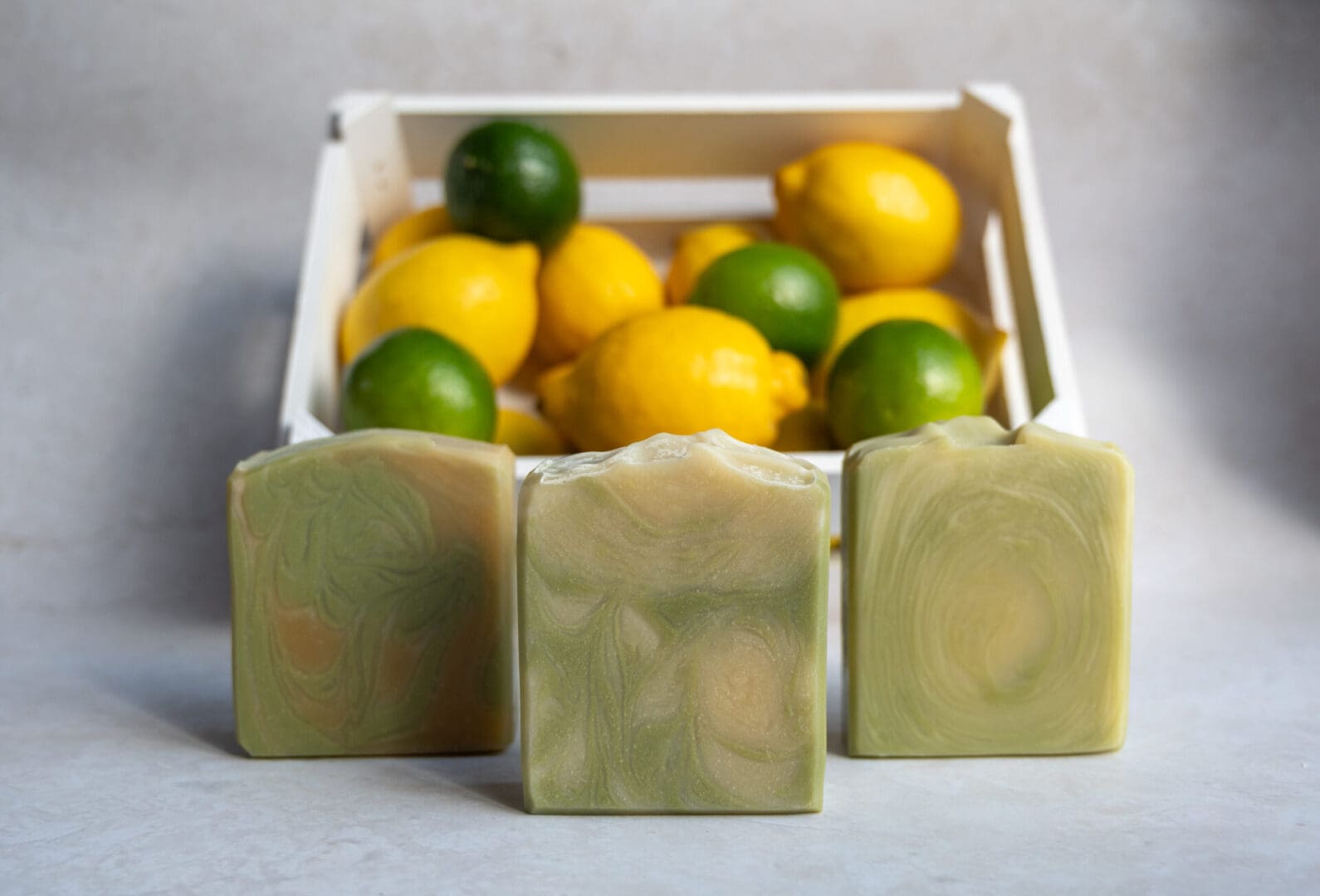 Green and yellow soap bars sitting in front of a crate full of lemons and limes
