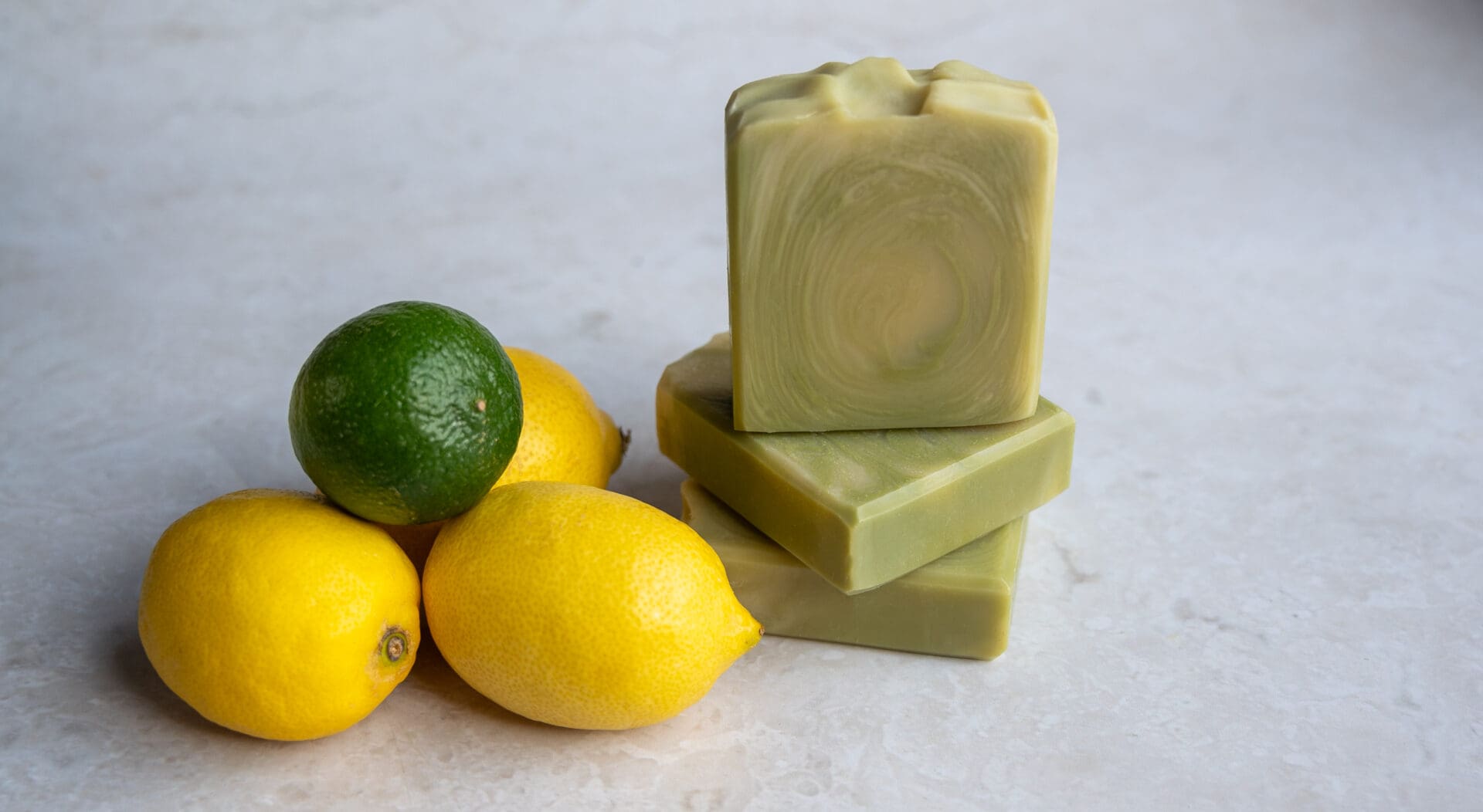 Green and yellow soap bars sitting next to lemons and limes