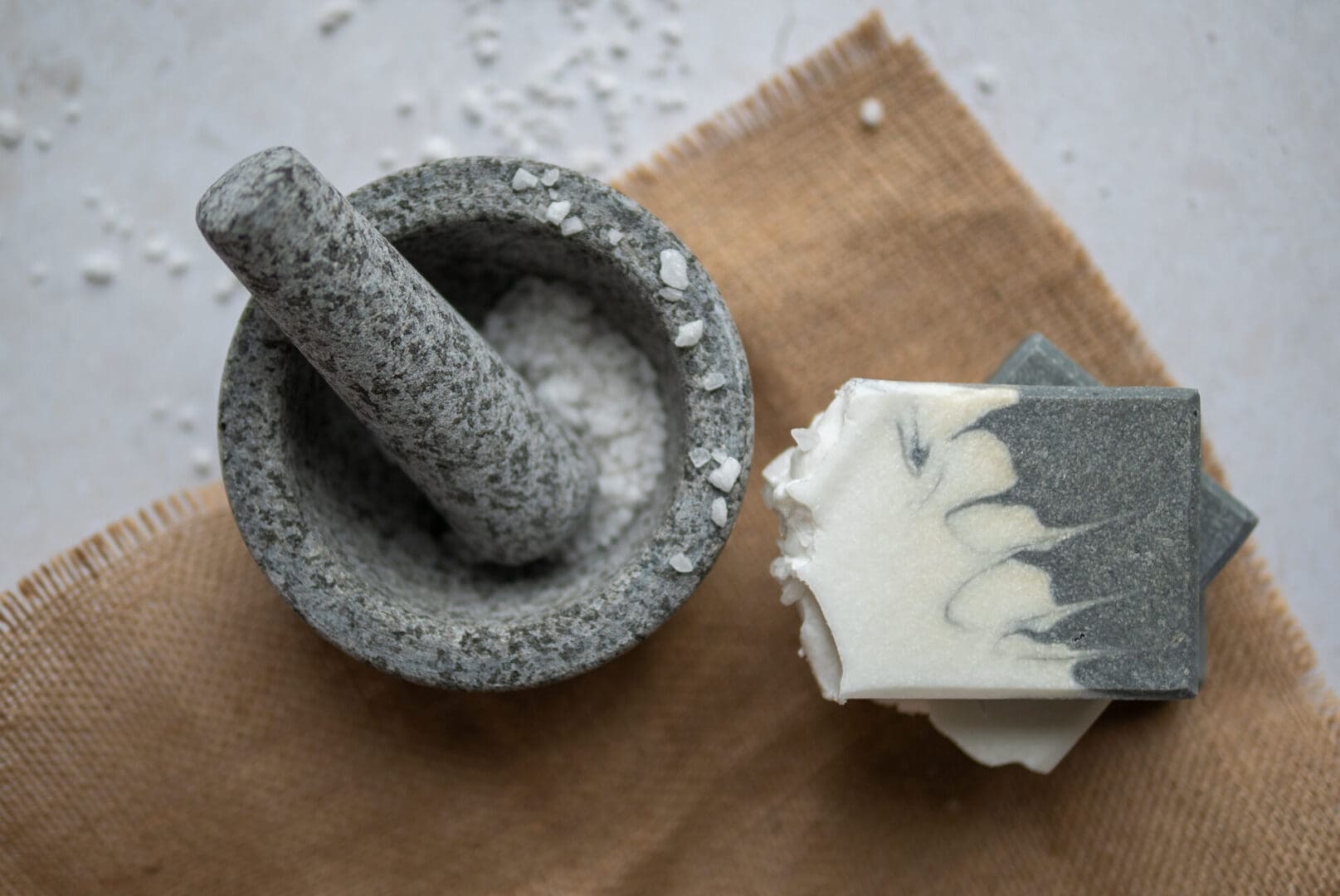 White and grey patterened soap bar sitting on a brown cloth with sea salt in a grinder