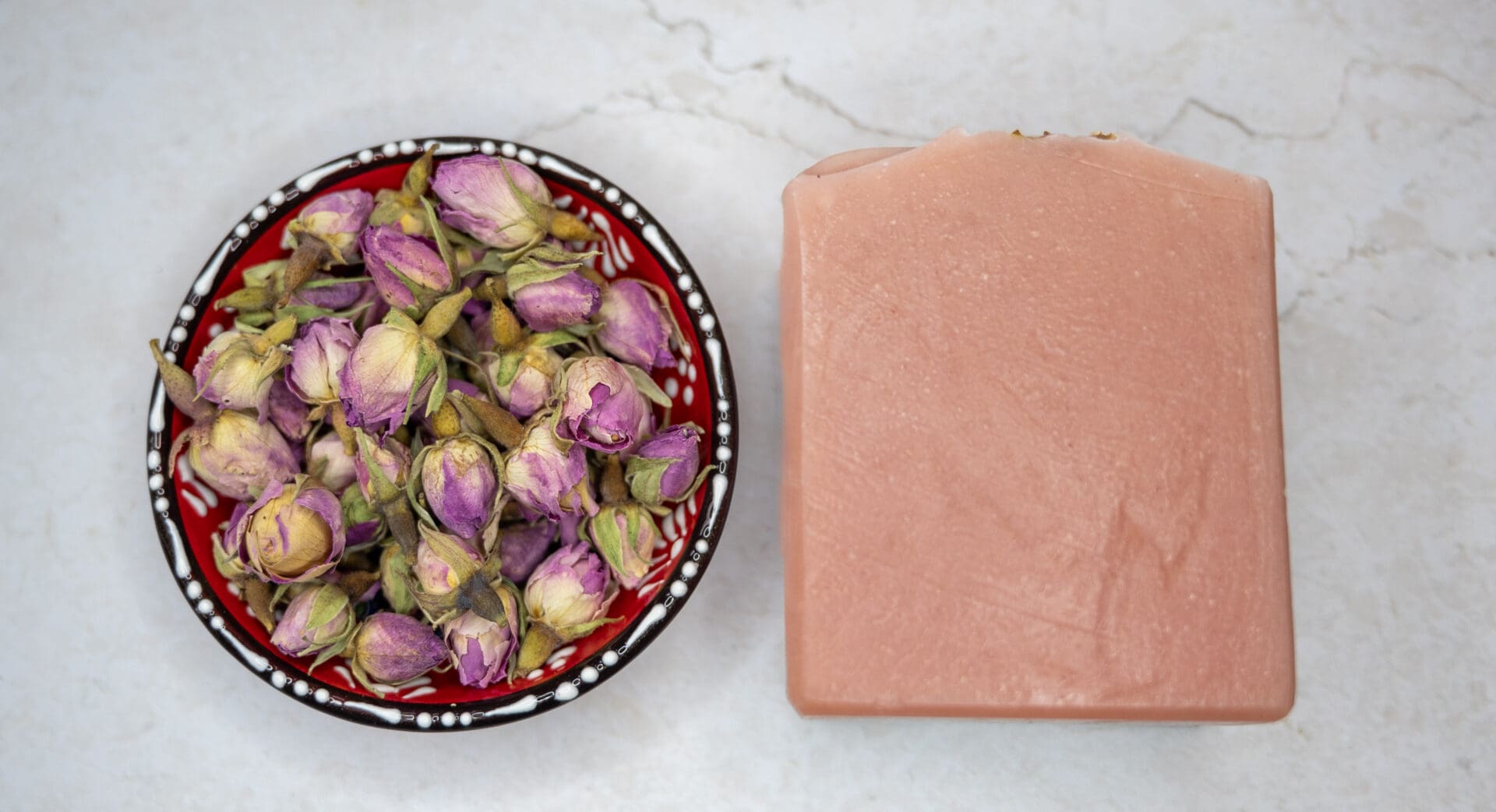 Pink natural soap bar next to a bowl of rose buds