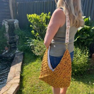 Stylish-urban-boho-tote-bag-hanging-from-a-woman’s -shoulder-featuring -a-woven-texture-with-earthy-tones- The-bag-has-a-slouchy-casual-shape-and-an-adjustable-strap