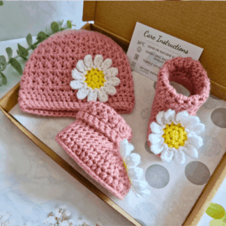 Handmade pink crochet baby hat and bootie set with white daisy flower details, displayed flat and suitable for a newborn.