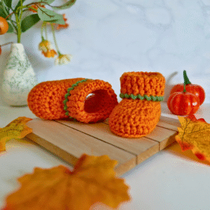 Handmade crochet pumpkin baby booties in orange with green twisted cuff, perfect for Halloween and autumn baby gifts.