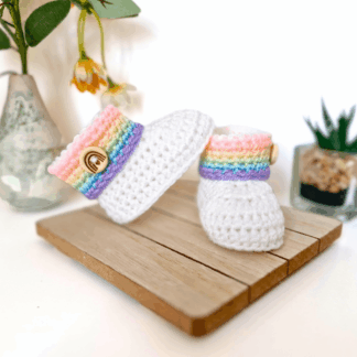 Handmade crochet baby booties in a soft cream yarn featuring a ribbed cuff and a round rainbow wooden button