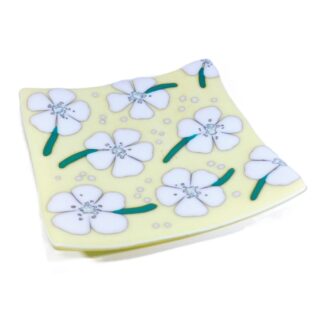 A fused glass platter with a scattering of daisy type flowers on a cream/vanilla base