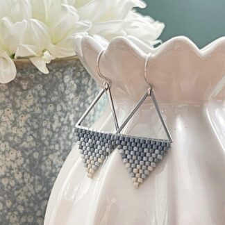 Geometric beaded earrings in shades of blue displayed on a ceramic vase