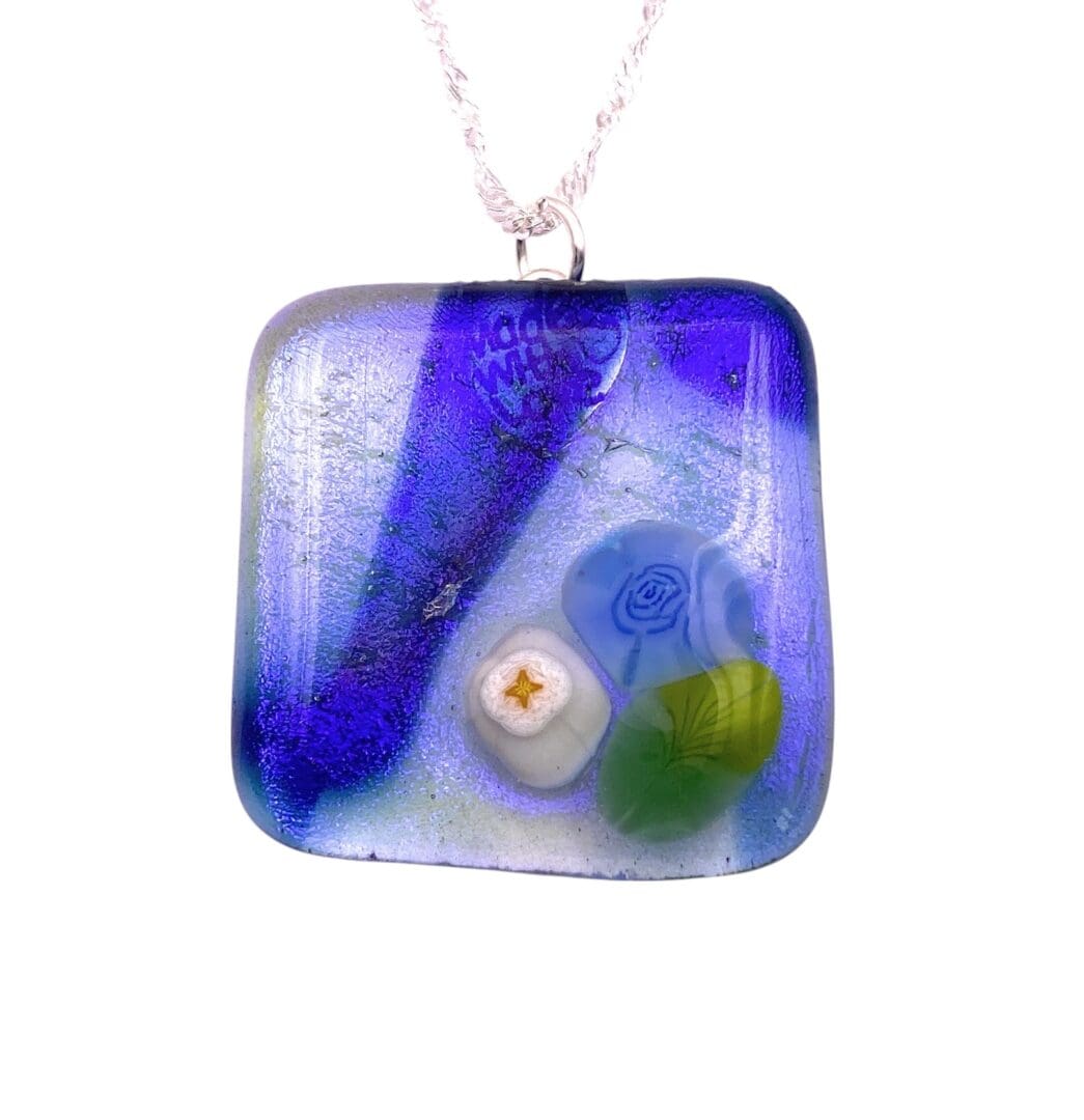 A colorful glass pendant featuring a mix of blues, greens, and whites with floral designs and a gold star, hanging from a silver chain.