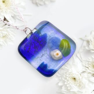 A vibrant blue glass pendant featuring floral designs, surrounded by white daisies on a light background.