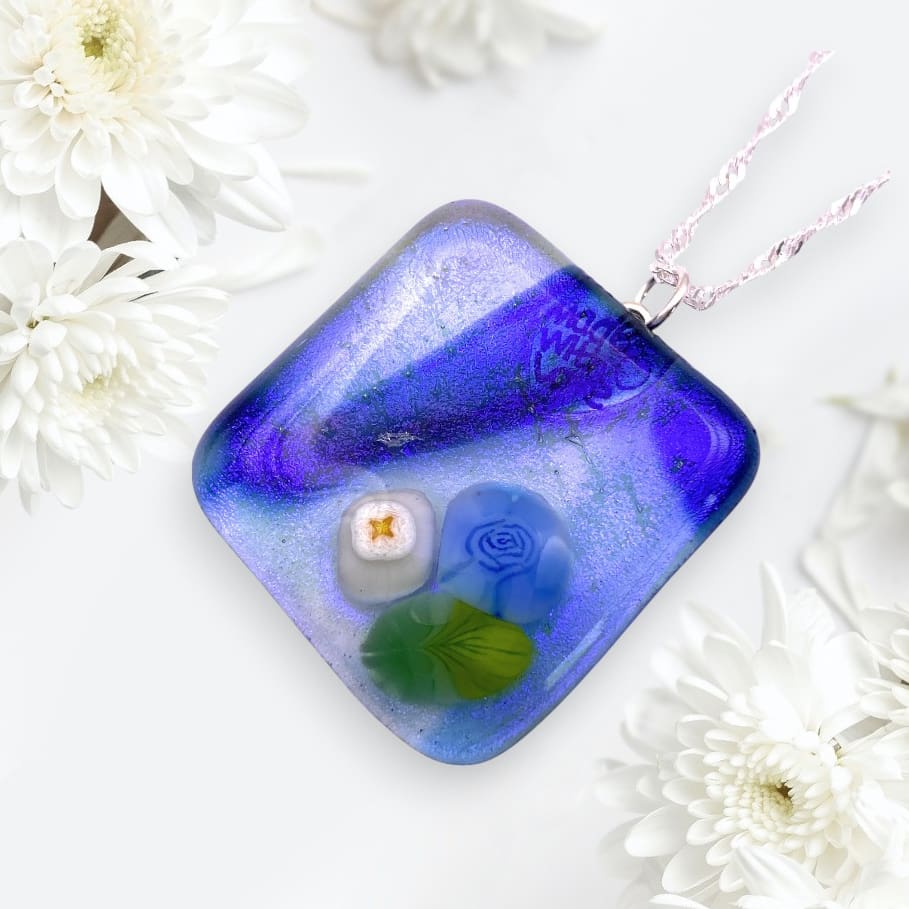 A vibrant blue glass pendant featuring floral designs and surrounded by white chrysanthemums, symbolizing elegance and nature.
