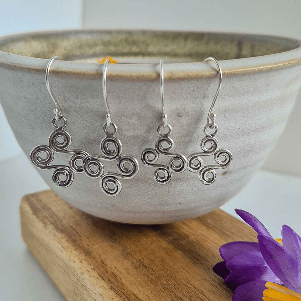 Two pairs of double-ended spiral earrings in sterling silver hanging off the edge of a bowl.
