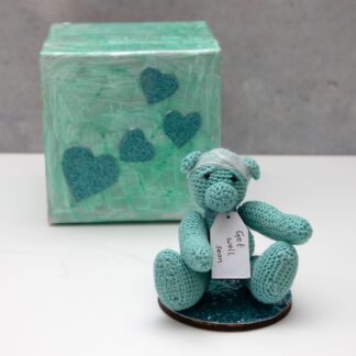small crochet bear in turquoise with bandage round his head with get well soon message