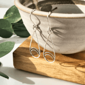 Handmade sterling silver teardrop earrings hanging off the edge of a bowl.