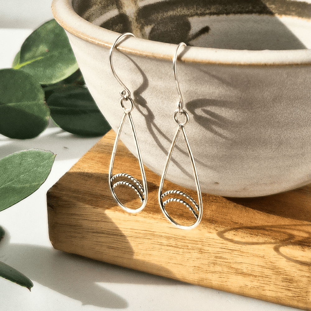 Handmade sterling silver teardrop earrings hanging off the edge of a bowl.