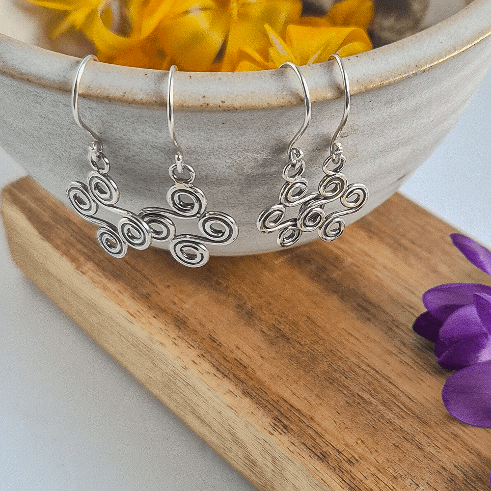 Two pairs of double-ended spiral earrings in sterling silver hanging off the edge of a bowl.