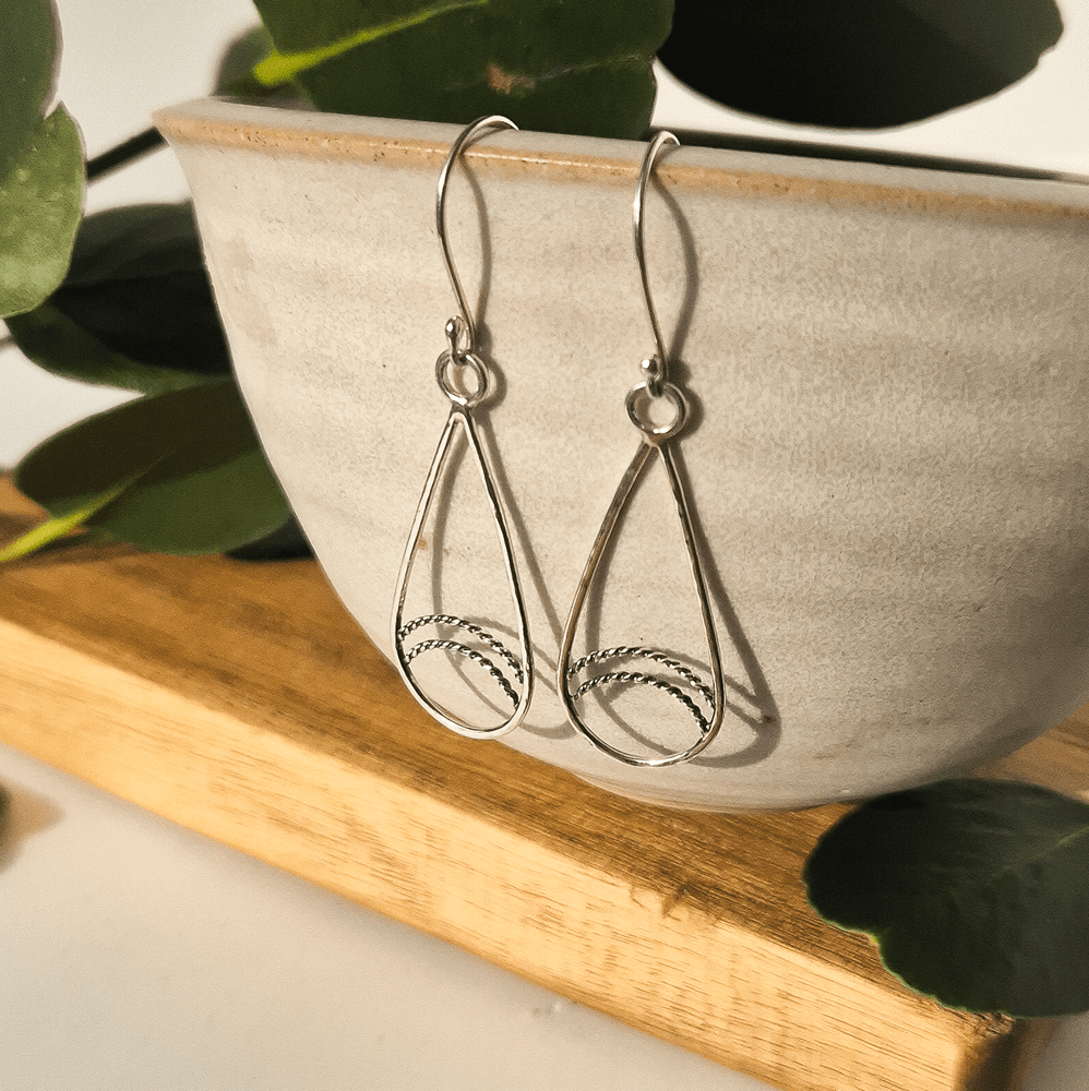 Handcrafted silver teardrop earrings hanging off the edge of a bowl