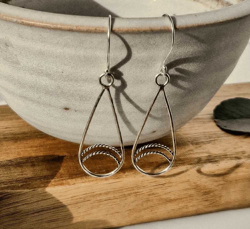 Silver teardrop earrings hanging via their shepherd's hooks off the edge of a bowl