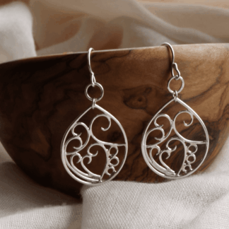 Teardrop sterling silver earrings with swirling central detailing hanging off an olive wood bowl.