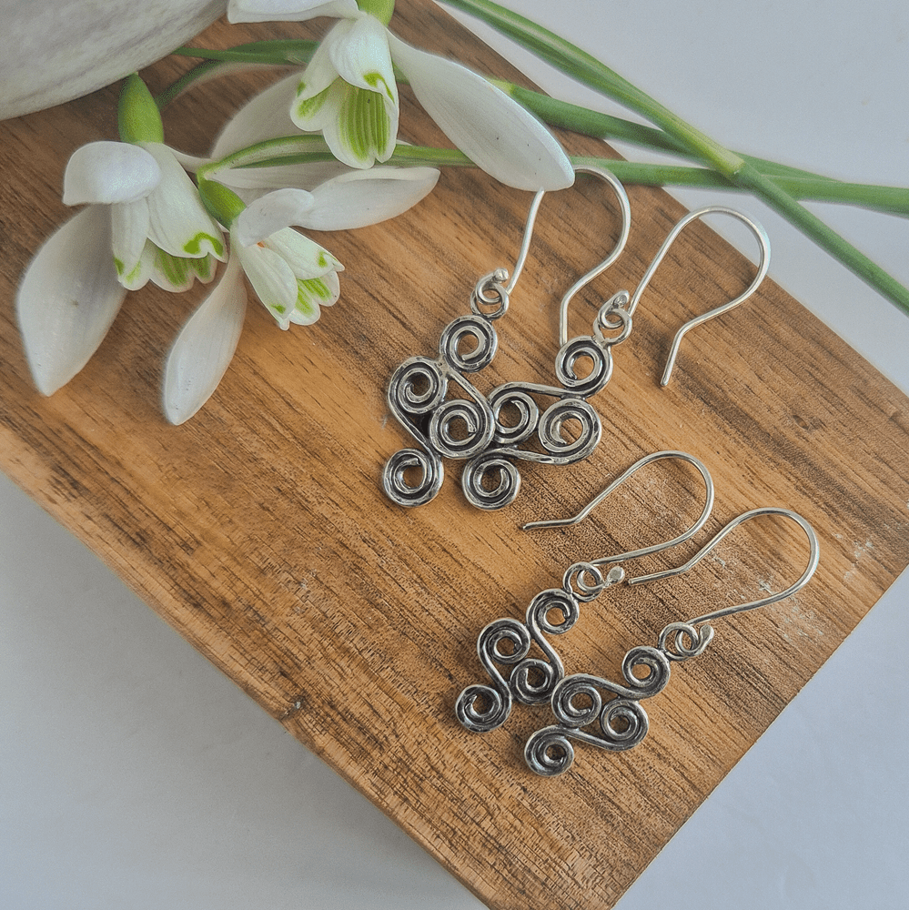 Overhead photo of two pairs of double-ended spiral earrings, with white snowdrops on the left.
