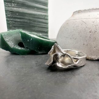 Sculpted silver ring sitting beside green wax in front of crucible