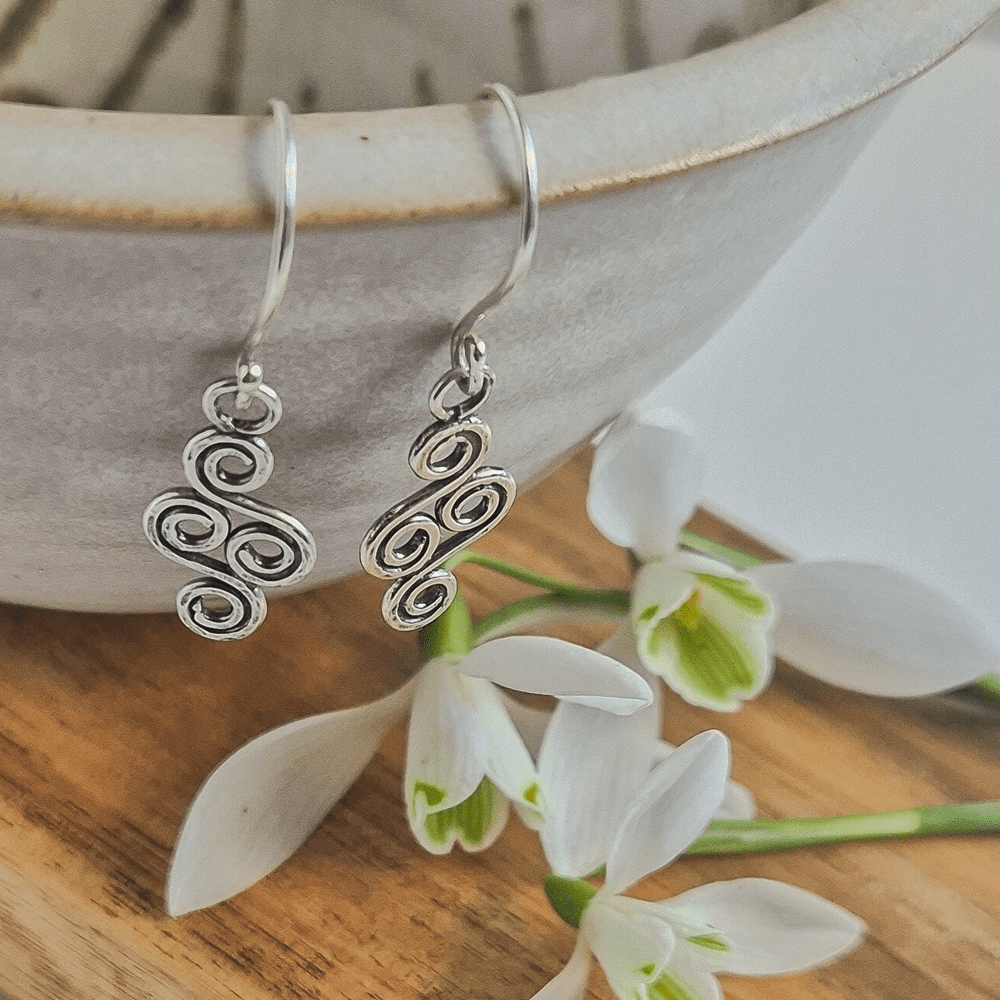 Small pair of double-ended spiral earrings hanging off the edge of a bowl.