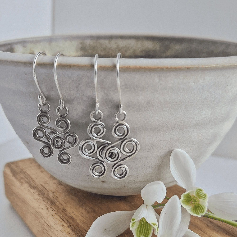 Two pairs of sterling silver double-ended spiral earrings hanging off a bowl, with white snowdrops in the foreground.