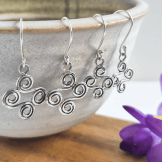 Two pairs of double-ended silver spiral earrings hanging off the edge of a bowl.