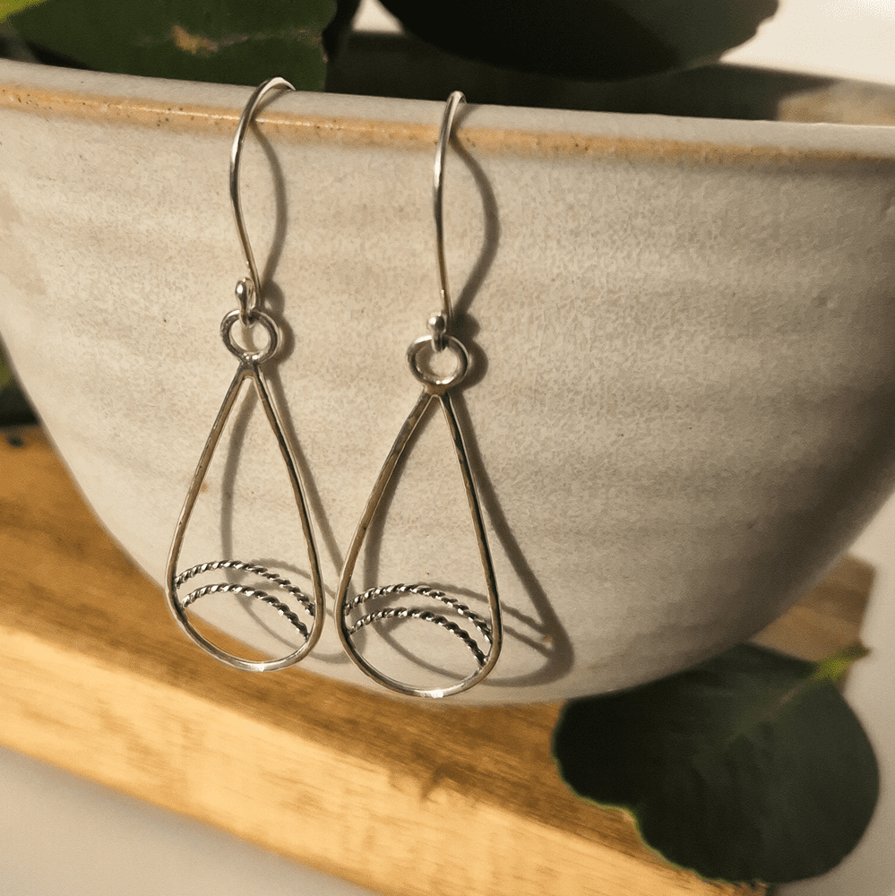 Handmade sterling silver teardrop earrings with twisted wire detailing hanging off the edge of a bowl