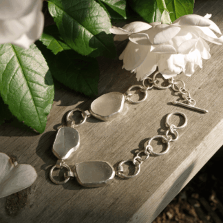 Triple seaglass and sterling silver bracelet resting on a piece of wood beside a rose in the sunlight.
