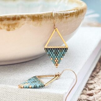 Gold and blue seed beaded triangle earrings displayed hanging from a ceramic dish