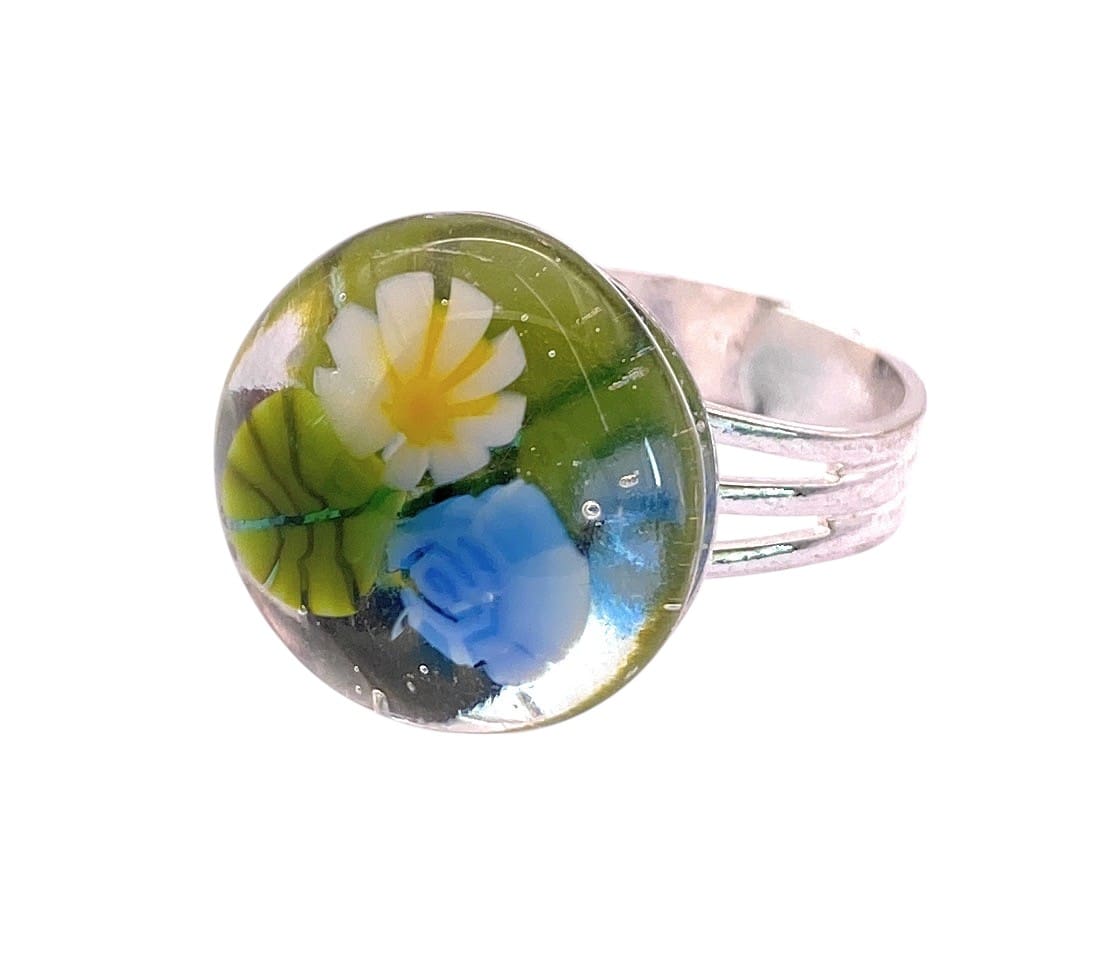 A colorful glass ring featuring a floral design with blue rose and a white and yellow daisy, set on a clear glass background.