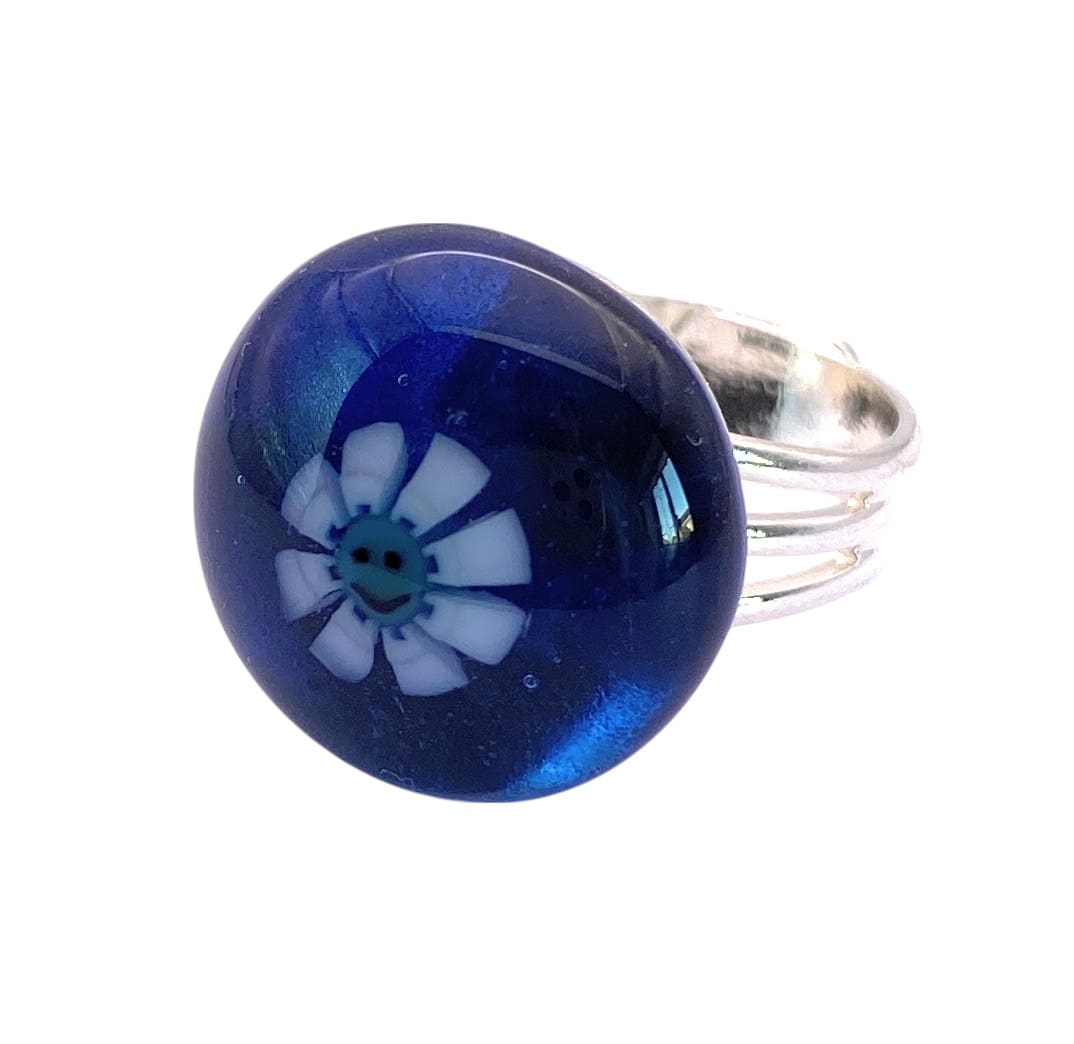 A blue glass ring featuring a white flower design with a smiling face in the center, set on a silver band.
