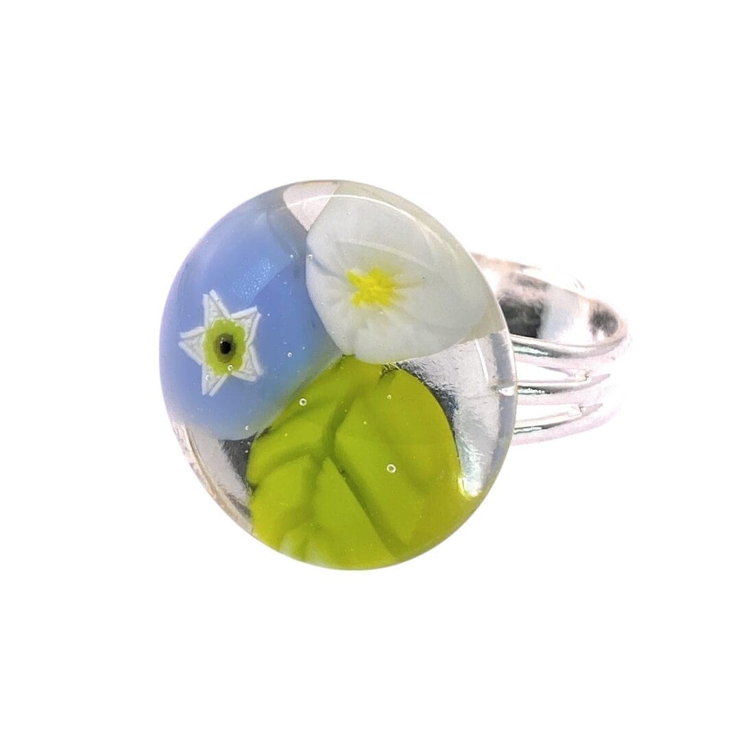 A colorful handmade glass ring featuring a blue flower with additional white flower and a green leaf.