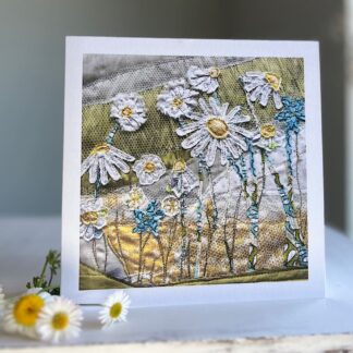 Textile art print of daisies on greetings card standing on table with real daisies