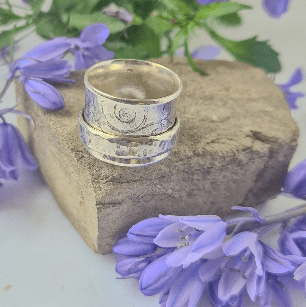 Sterling silver handcrafted spinner ring resting on a rock, surrounded by purple/blue flowers.