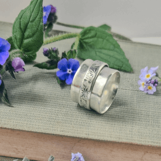 Handmade sterling silver spinner ring with floral motif resting on its side on top of a green hardback book.