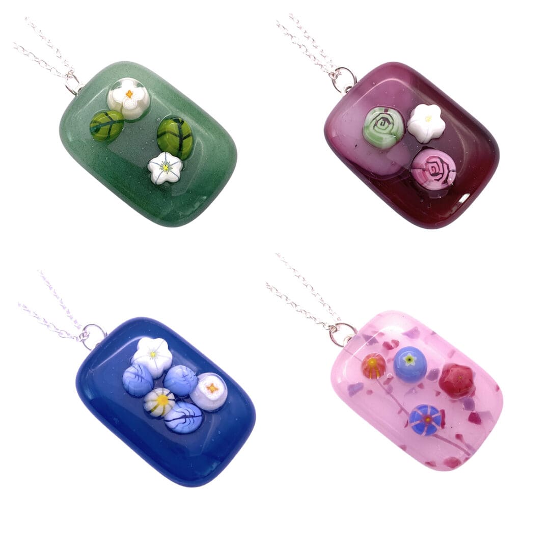 Four colorful handmade glass pendants featuring intricate floral three dimensional designs on green, fuchsia, blue, and pink, attached to silver chains.