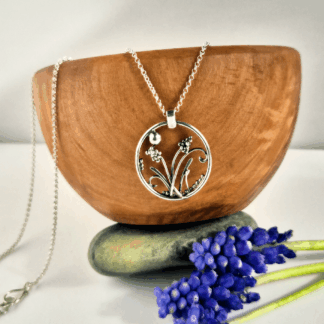 Circular sterling silver pendant with wildflowers inside, hanging off an olive wood bowl.