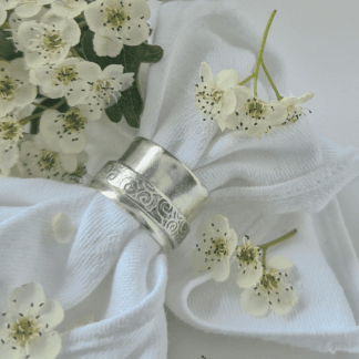Chunky sterling silver spinner ring displayed on white cloth and surrounded by white flowers.