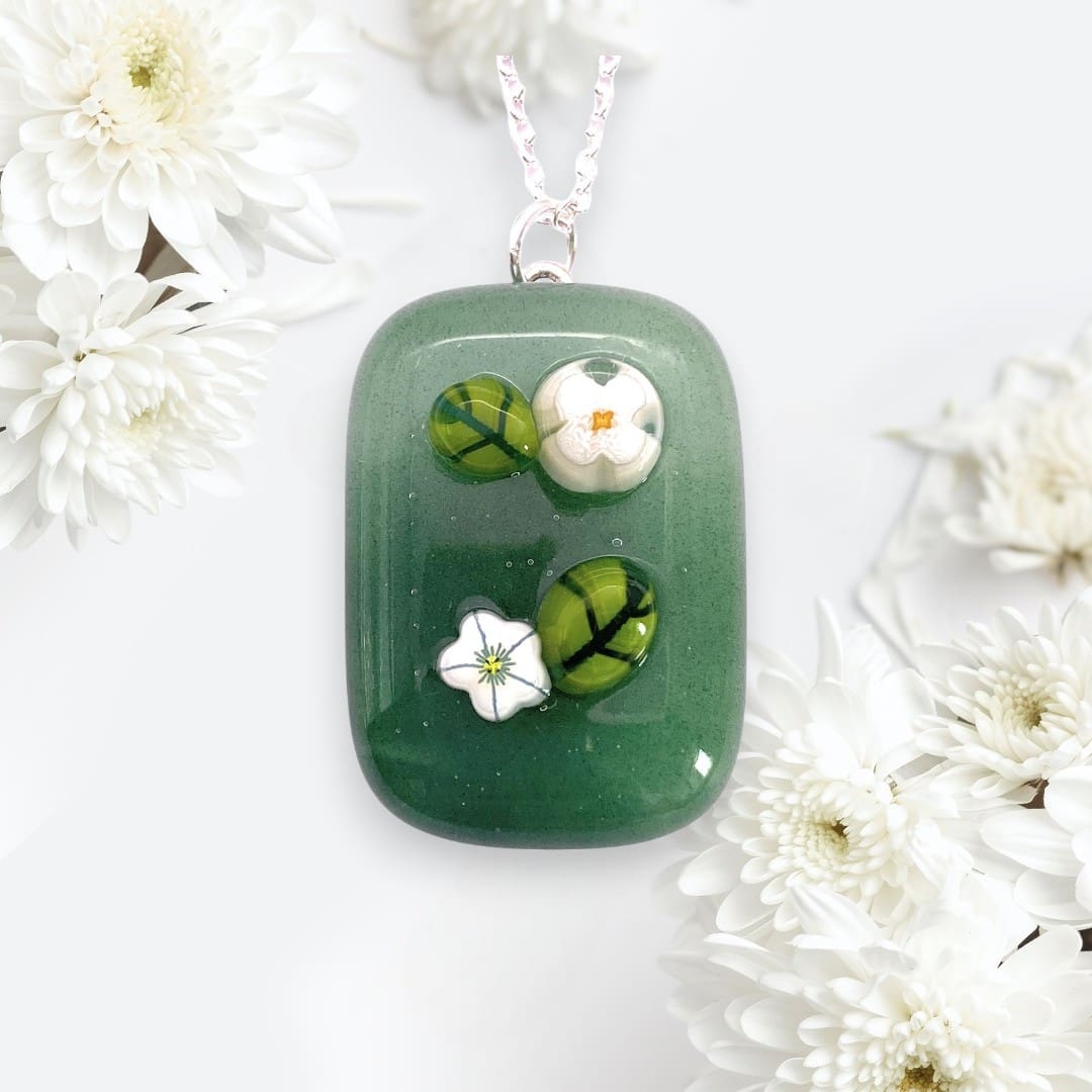 Green handmade glass pendant with three dimensional floral designs, featuring two green leaves and two white flowers, surrounded by white daisies.