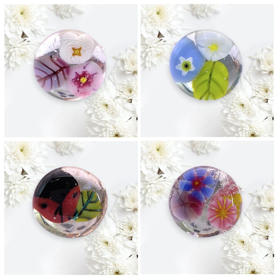 Four intricately designed handmade glass rings featuring vibrant flowers and intricate patterns, surrounded by white chrysanthemums.