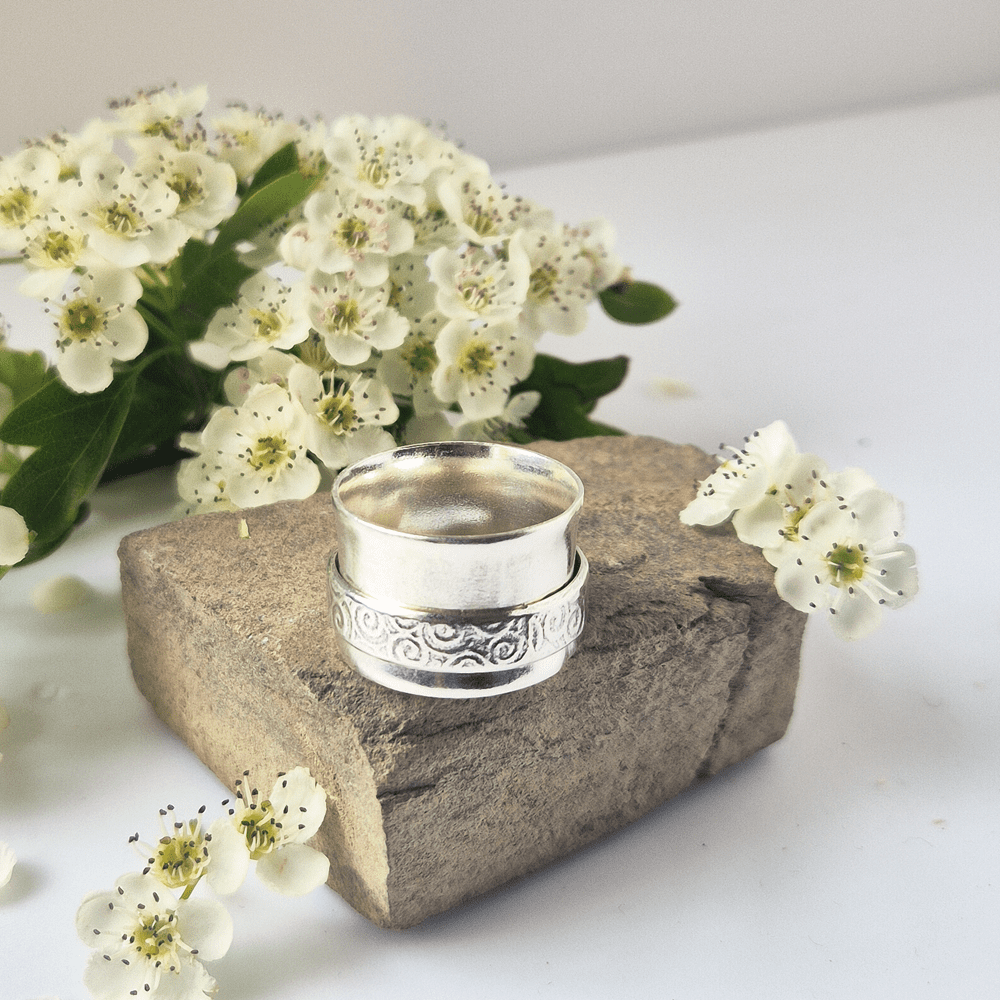 Sterling silver spinner ring resting on a piece of rock, surrounded by white flowers.