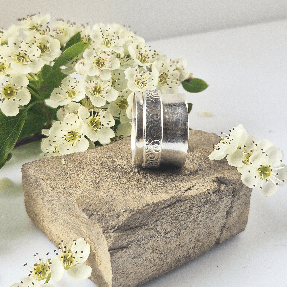 Sterling silver spinner ring resting on its side on a piece of rock, surrounded by white flowers.