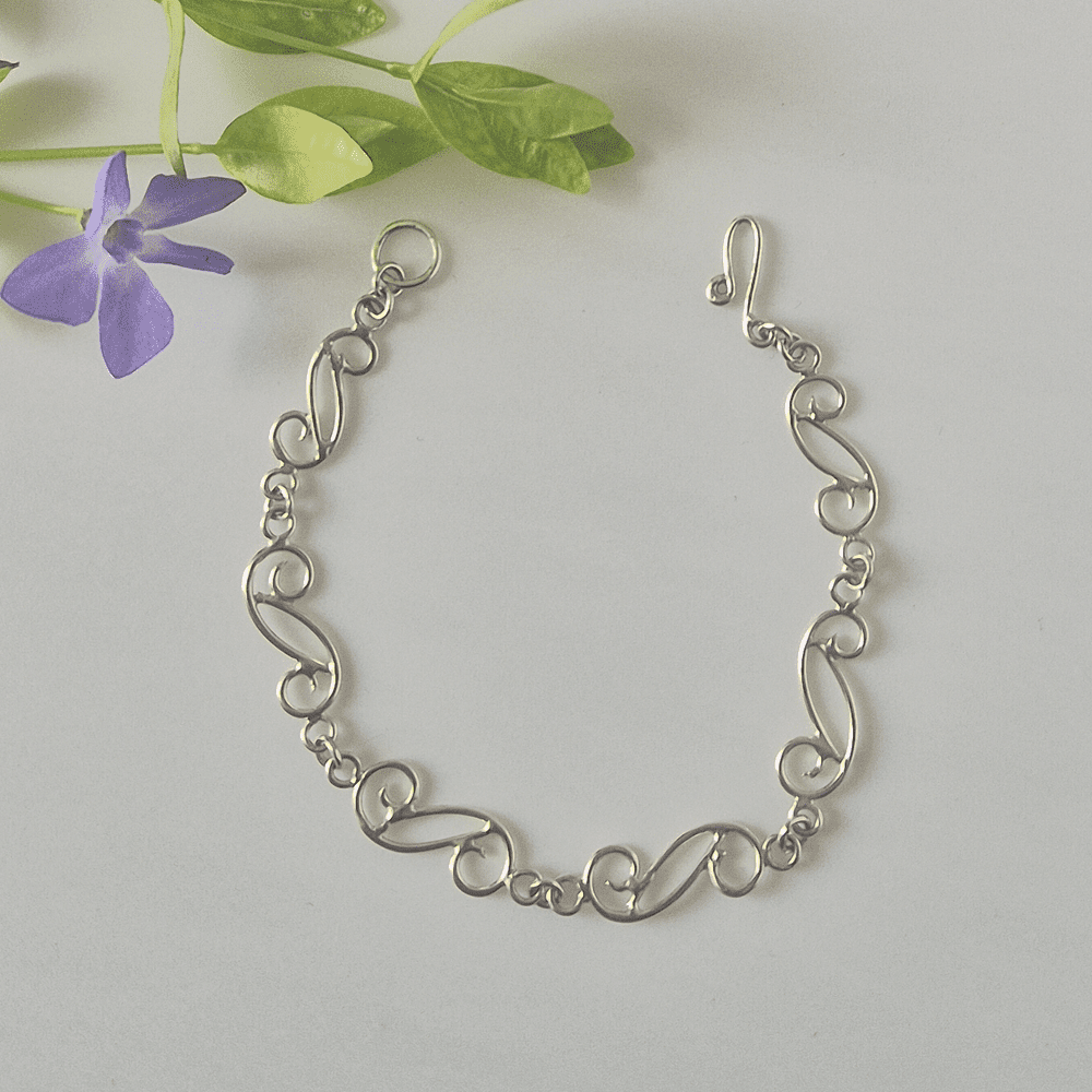 Overhead photo of the sterling silver spiral wave bracelet with a purple flower nearby.